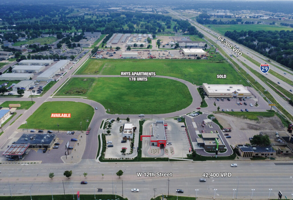 South view aerial of the available parcel at the Crossroads Development, with W. 12th Street retail in the foreground and the I-29 corridor beyond