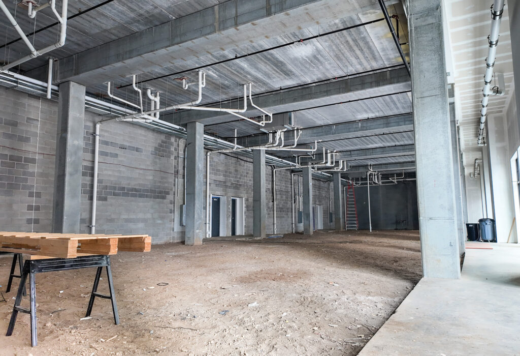Steel District retail for lease shell with exposed utilities, concrete columns and an unfinished open floor area.