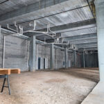 Steel District retail for lease shell with exposed utilities, concrete columns and an unfinished open floor area.
