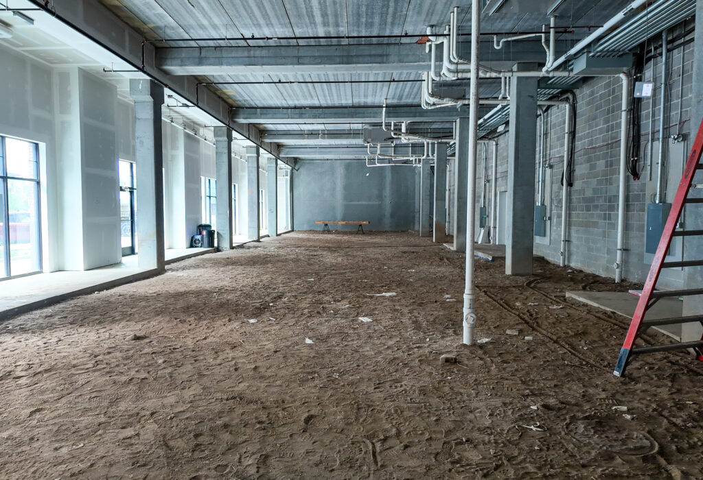 Long interior view of Steel District retail for lease shell with storefront windows and exposed building systems.