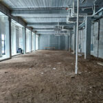 Long interior view of Steel District retail for lease shell with storefront windows and exposed building systems.
